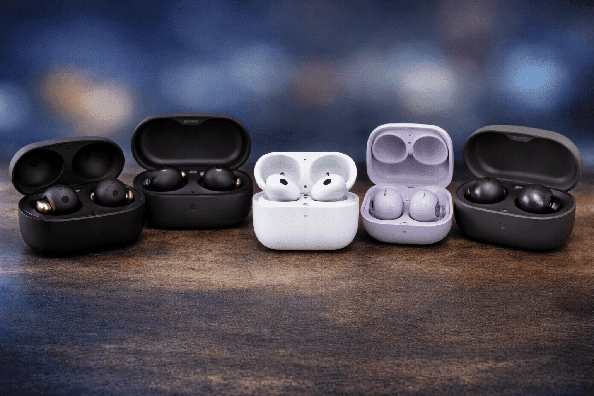 Close-up of multiple wireless earbuds in open charging cases placed side by side on a table with a blurred background, showcasing modern design and premium build quality.